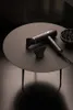A black hairdryer and its attachments are displayed on a dark, round table. Podgląd zdjęcia produktu