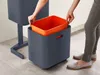 A person is placing an orange inner bin into a larger graphite bin. Podgląd zdjęcia produktu