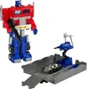 A red and blue Optimus Prime action figure stands to the left of a grey docking station with a blue robotic arm and a silver vehicle. Produktbild-Vorschau