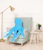 A blue plush octopus sits in a light blue armchair next to a small side table with a vase and a clock. Náhľad obrázku produktu