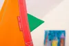A close-up of a colorful hanging chair with tags, with a painting in the background. Produktbild-Vorschau