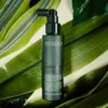 A dark green bottle of Natucain hair serum is placed on a background of large green leaves. Produktbild-Vorschau
