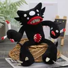 A black plush toy monster with red and white accents sits on a woven basket, with a plant and a small chalkboard in the background. Produktbild-Vorschau