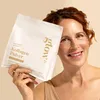 A woman holds a package of collagen powder and smiles at the camera. Produktbild-Vorschau