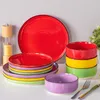 A collection of colorful ceramic plates and bowls arranged on a white surface, with a salt and pepper grinder in the background. Náhled obrázku produktu
