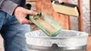 A person is emptying dust from a Bosch tool into a trash can, while holding a filter. Produktbild-Vorschau