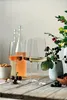 Three wine glasses filled with different colored wines, along with bottles, berries, nuts, and a vase with flowers, are arranged on a wooden table. Náhled obrázku produktu