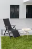 A black recliner chair and a small round table are placed on a patio next to a grassy area. Produktbild-Vorschau