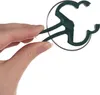 A hand holding a green plant clip against a white background. Voir les images du produit