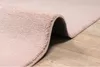A close-up view of a pink rug with a textured surface, partially rolled up, resting on a wooden floor. Produktbild-Vorschau
