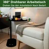 A black C-shaped side table with a tablet, fruit, and a mug of milk on it, placed next to a beige armchair with a blanket. Produktbild-Vorschau