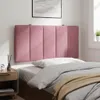 A pink upholstered headboard is mounted on a white wall above a bed with white and gray bedding. A wooden nightstand with a clock and diffuser is to the left of the bed. Produktbild-Vorschau