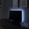 A television with LED backlighting mounted on a wall above a media console in a dimly lit room. Produktbild-Vorschau