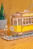 A close-up of a wooden model tram on a wooden surface, with a plant in a pot in the background. Produktbild-Vorschau