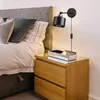 A bedroom scene with a bed and a nightstand, featuring a wall-mounted lamp. Náhľad obrázku produktu