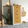 A narrow chest of drawers with wooden fronts, a woven bag, and shoes on a patterned floor, next to a mirror reflecting a lamp. Produktbild-Vorschau