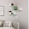 A white corner shelf unit with books and a plant displayed on it, positioned on a light gray wall above a sofa with patterned pillows. Podgląd zdjęcia produktu