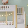A close-up view of a white and natural wood bunk bed with drawers and stairs. Produktbild-Vorschau