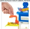 A hand is shown pulling a lever on a Hot Wheels City Hai-Angriff Spielset, with a yellow toy car on a platform. Produktbild-Vorschau