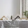 A table set with multiple candle holders and lit candles, with a chair in the foreground. Podgląd zdjęcia produktu
