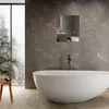 A modern bathroom with a large window overlooking a snowy landscape, featuring a freestanding bathtub and marble-tiled walls. Produktbild-Vorschau