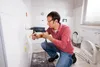 A man is drilling a hole in a tiled wall in a bathroom. Podgląd zdjęcia produktu