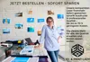 A woman is standing in front of a brick wall with photos pinned to it, leaning on a table with printing equipment and photos. Produktbild-Vorschau