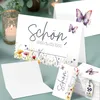 A table setting with cards, a candle, and greenery. Produktbild-Vorschau