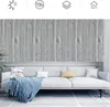 Graue Holzmaserungs-Tapete an einer Wand über einem hellgrauen Sofa mit blauer Decke und Kissen Náhled obrázku produktu