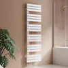 A white designer towel radiator is mounted on a light brown wall in a bathroom setting, with a large green plant to the left and a shower enclosure to the right. Podgląd zdjęcia produktu