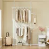 A bedroom setting with a telescoping clothes rack filled with clothes, a suitcase, and a nightstand. Náhľad obrázku produktu