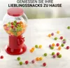 A red gumball machine filled with colorful candies sits on a white surface, with scattered candies around it. Náhled obrázku produktu