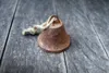 A rusty, small bell with a rope attached, lying on a weathered wooden surface. Náhľad obrázku produktu