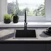 A modern kitchen sink with a black faucet and a view of greenery through the window. Náhled obrázku produktu