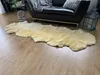 A sheepskin rug is laid out on a wooden floor in front of a black leather sofa. A decorative lantern is placed next to the sofa. Produktbild-Vorschau