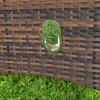 A close-up view of a wicker-like textured surface with a silver handle, set against a background of green grass. Produktbild-Vorschau