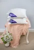 Two white pillows are stacked on a chair draped with a pink blanket. A small bouquet of white flowers in a vase sits to the left of the chair. Produktbild-Vorschau