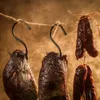 Several pieces of smoked meat and sausages are hanging from hooks on a string, with a smoky, warm background. Podgląd zdjęcia produktu