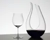 A clear glass wine glass and a wine decanter filled with red wine are displayed on a dark surface against a white background. Podgląd zdjęcia produktu