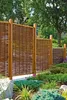 A garden fence made of woven willow branches with wooden posts, surrounded by lush green plants and flowers. Produktbild-Vorschau
