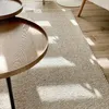 A close-up view of a textured rug with sunlight casting shadows, next to a wooden coffee table. Voir les images du produit