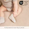 A close-up of a baby's legs and feet, wearing socks, on a textured beige surface. Produktbild-Vorschau