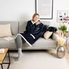 A woman is sitting on a couch wearing a dark blue hoodie blanket. Produktbild-Vorschau