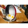 A hand is holding a frying pan with two fried eggs, tilting it over a plate. Podgląd zdjęcia produktu