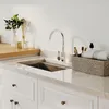 A modern kitchen sink area with a chrome faucet, marble countertop, and white cabinets. Produktbild-Vorschau
