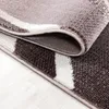 A close-up, folded view of a modern abstract wave design carpet with brown, white, and gray patterns. Náhľad obrázku produktu