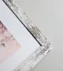 A close-up view of a distressed white picture frame with a floral image visible behind it. Produktbild-Vorschau