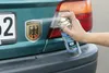 A hand sprays a cleaning product onto a car's rear bumper near a license plate and taillight. Produktbild-Vorschau