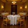 A dimly lit dining room or banquet hall with round tables set for a meal. Produktbild-Vorschau