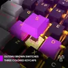 A close-up view of a gaming keyboard with purple and black keycaps, illuminated by yellow and purple backlighting. Produktbild-Vorschau